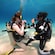 Two women in scuba diving gear kneeling on a sandy ocean floor